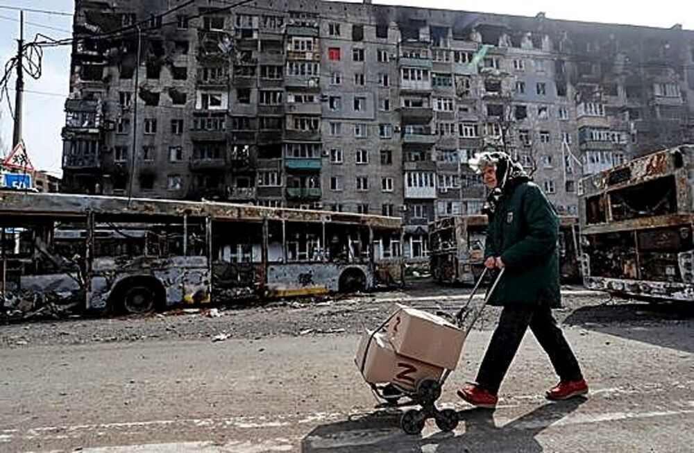 Una residente transporta un carro con ayuda humanitaria frente a un edificio destruido por los ataques. 